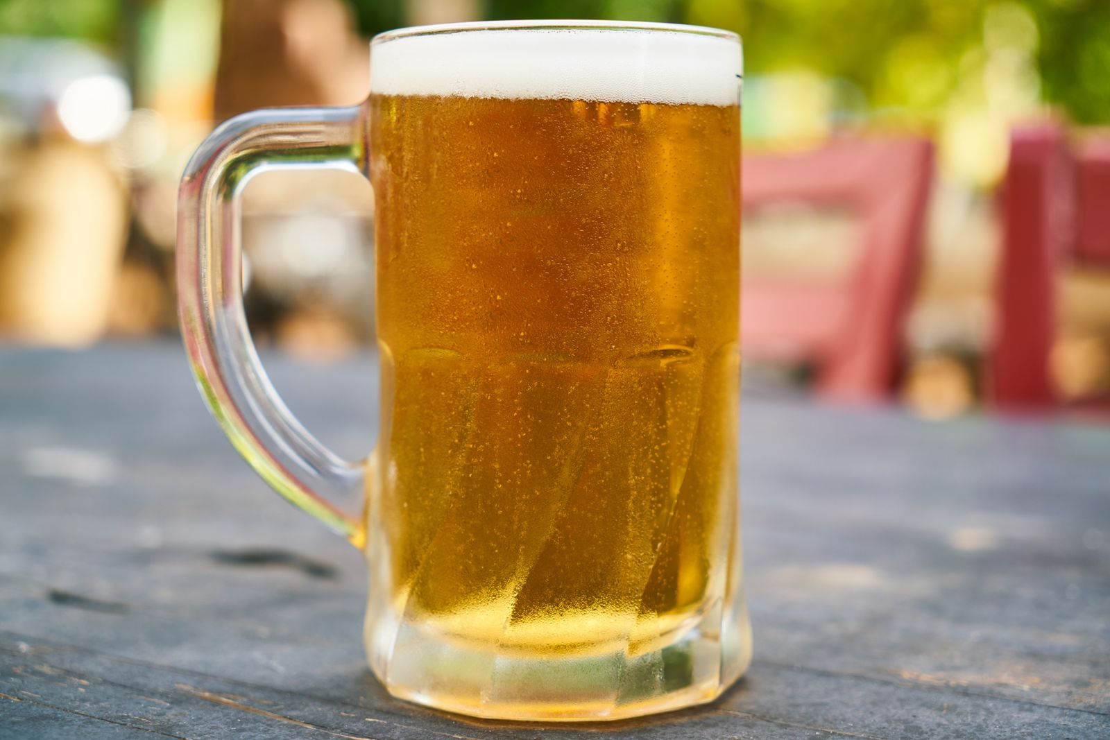 A pint of golden beer on a wooden table in a sunny pub beer garden, representative image